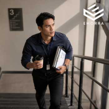 Lelaki pejabat menaiki tangga sambil membawa dokumen kerja dan secawan kopi dalam suasana profesional.