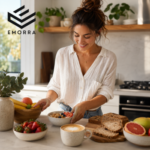 Seorang wanita sedang menyediakan sarapan sihat di dapur moden dengan semangkuk oat, buah-buahan, roti gandum dan secawan kopi, menggambarkan amalan pemakanan tinggi serat untuk gaya hidup yang lebih sihat.